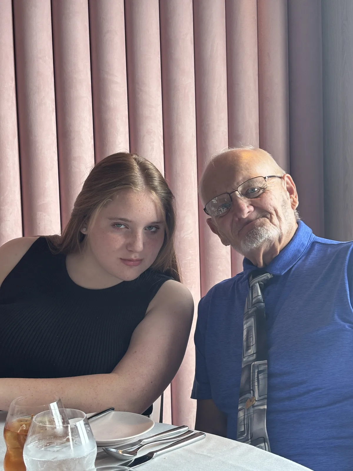 Dennis Myers sits at a dinner table in a blue shirt and tie beside one of his grandchildren.