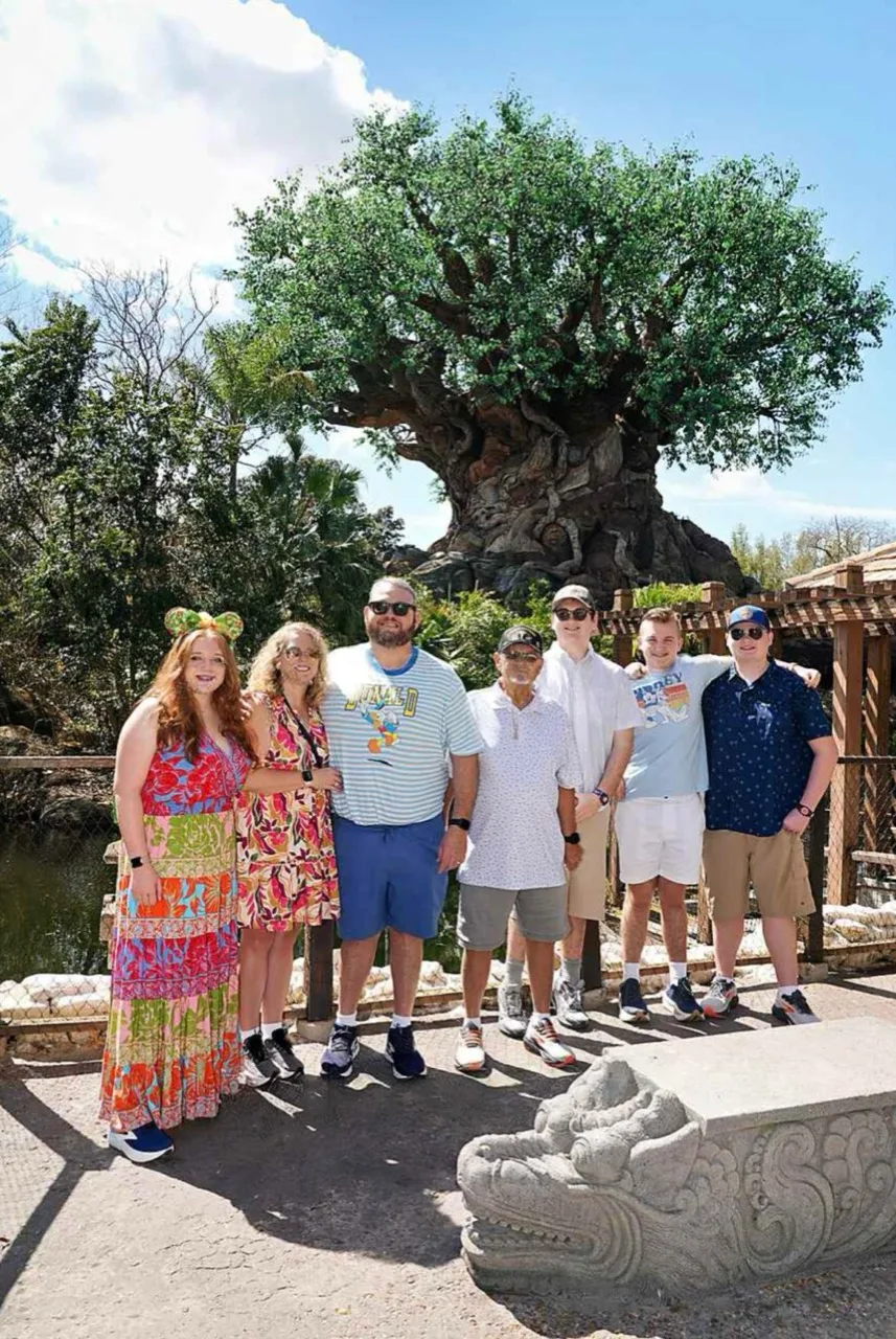 Dennis Myers stands with six family members in front of a large tree.