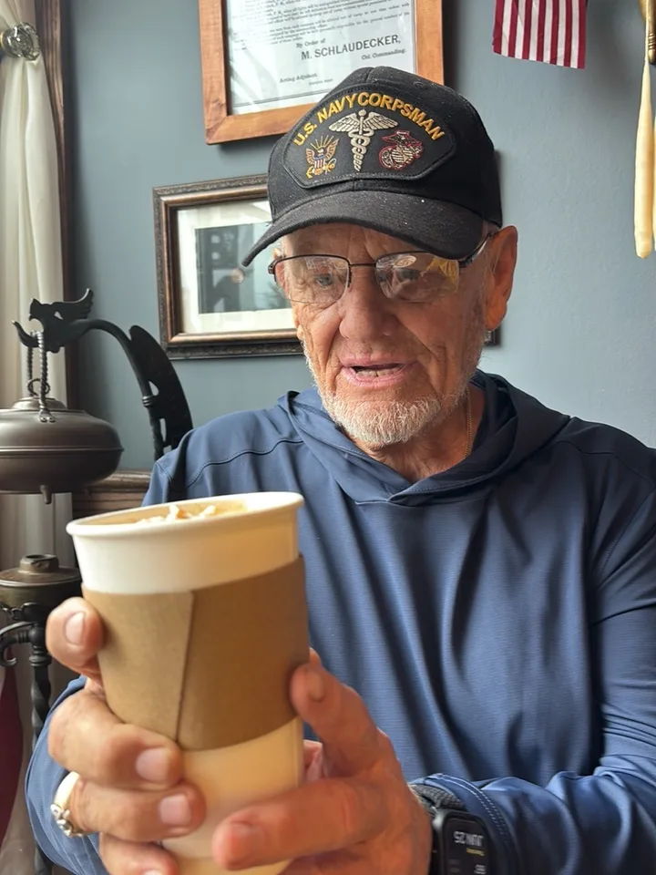 Dennis Myers looks down at a paper coffee cup held in both hands inside Enlisted Coffee.